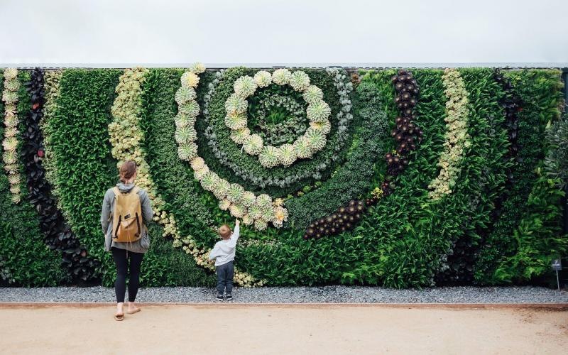 mother and child standing in front of a mural made of plants